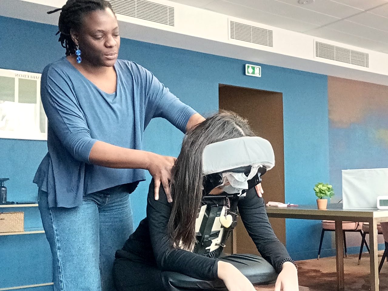 Séance de massage assis en entreprise : la praticienne travaille la nuque d’une salariée installée sur la chaise ergonomique.